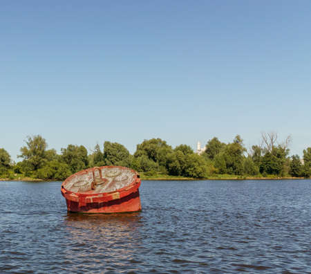 Old red buoy marks the fairway at entrance to port. Sunny day. Copy space