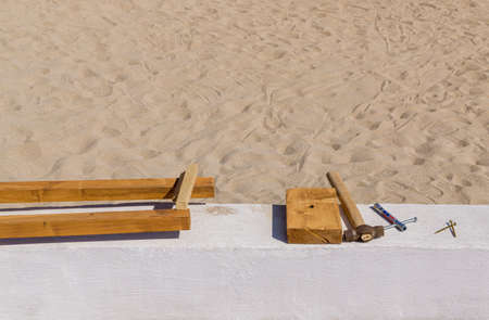 Old hammer, screws and wooden work pieces lie on the concrete parapet near sandy beach. Sunny day....