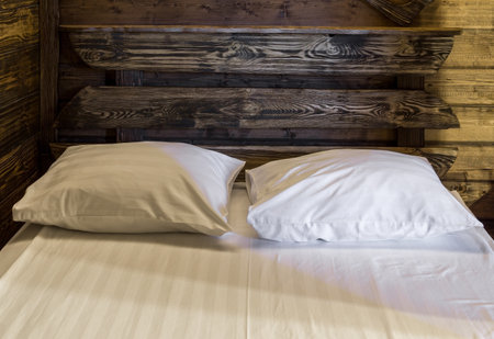 Bedroom interior evening. Fragment of wooden double bed with mattress, pillows and sheet. Walls of room are covered with wooden panelsの写真素材