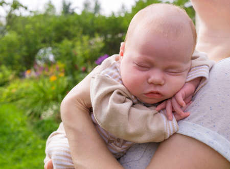 Portrait of newborn baby of european type sleeping in arms of his motherの写真素材