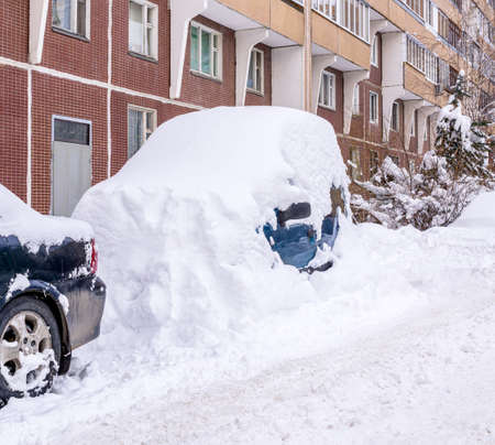 Car completely covered with snow after heavy snowfall is in courtyard of residential building. Copy spaceの写真素材