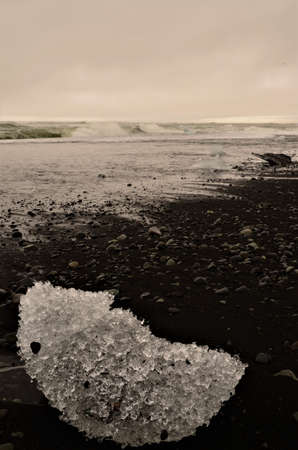 A view of iceberg fragments on a black sand beach with crashing waves at the glacial lagoon in...