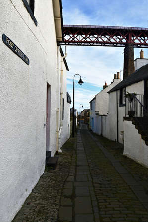A view along an old cobbled lane and the Forth railway bridge which towers over the historic town of North Queensferryの写真素材