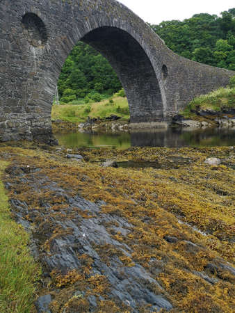 A view of the old stone bridge over the Atlantic. A narrow stretch of the Atlantic ocean that separates mainland Scotland from the island of Seil.の写真素材