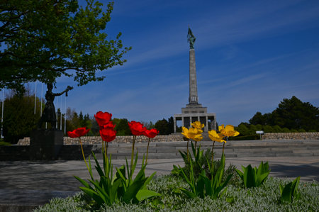 A view of the war memorial monumental architectural column among some formal gardens with vibrant flower beds and elegant statues in the city of Bratislava in Slovakia.の写真素材
