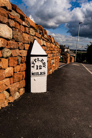 A A mile marker on a road outside a new housing estate on the outskirts of Penrith Cumbria United Kingdom showing 12 miles to Applebyの写真素材
