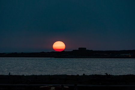 The sun low on the horizon on the coast line of Paphos on the island of Cyprusの写真素材