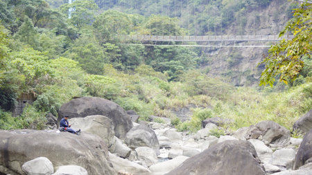 A man is sitting on a rock at the edge of the river.の写真素材