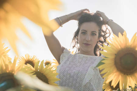 Young caucasian woman with long hairs among sunflowers fieldの写真素材