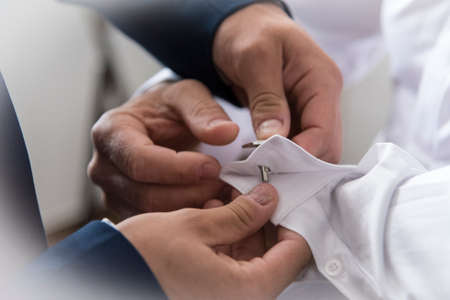 A groom putting on cuff-links as he gets dressed in formal wear. Groom's suit