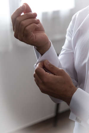 A groom putting on cuff-links as he gets dressed in formal wear. Groom's suitの写真素材