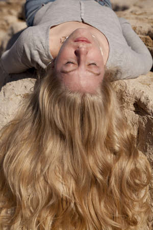 A woman laying on a rock with her hair flowing down the rock with her eyes closed.の写真素材