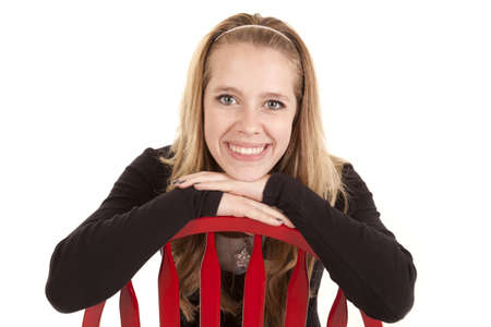 a teenage girl with her chin on the back of a red chair with a smile.の写真素材
