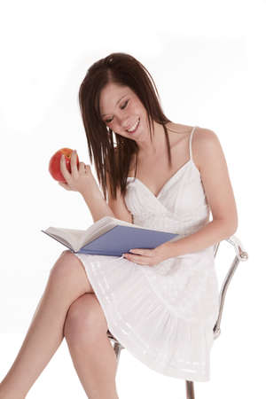 a woman sitting on her stool reading a book and holding a piece of fruit with  a smile on her face.の写真素材
