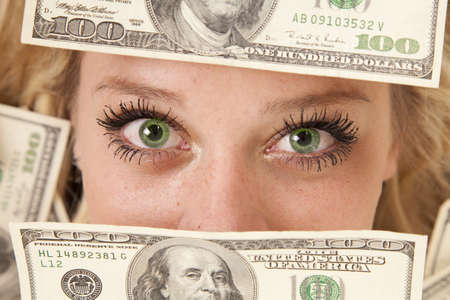 A woman with green eyes peeking through moneyの写真素材