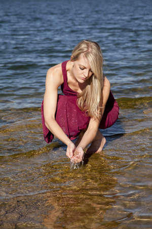 A woman in her formal dress bending down and playing with the water.の写真素材