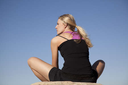 A woman stretching with her back to the camera in the outdoors.