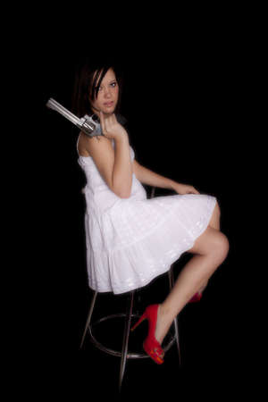 A woman sitting on a stool holding a gun with  a serious expression on her face.の写真素材