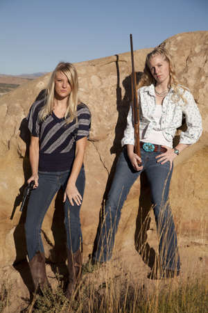Two women standing together holding their weapons in their western outfits.の写真素材