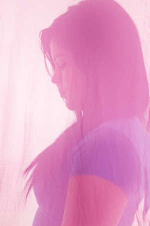 a teen girl looking down with a serious face hiding behind a pink piece of material.の写真素材