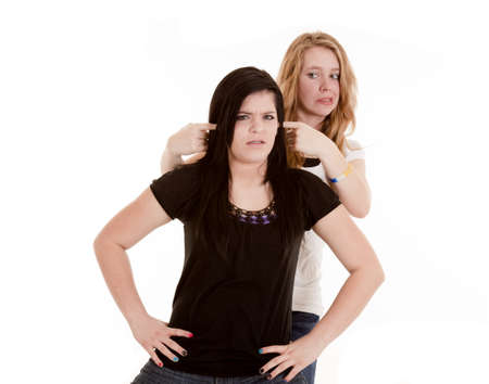 A teen plugging another teens ears with a funny expression on her face.の写真素材