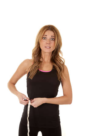 A woman measuring her waist with a scared expression on her face.の写真素材