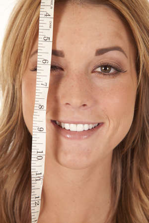 A woman with a measuring tape over one of her eyes with a smile on her face.の写真素材