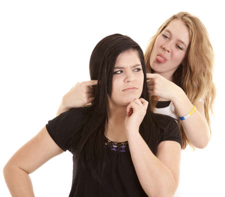 a teen with her fingers in her friends ears sticking out her tongue.の写真素材