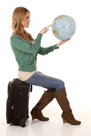 A woman sitting on her suitcase holding on to a world globe pointing out where she wants to go.の写真素材