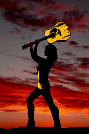 a silhouette of a woman getting ready to smash her guitar.の写真素材