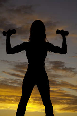 A silhouette of a  woman lifting weights with a beautiful sunset in the background.の写真素材