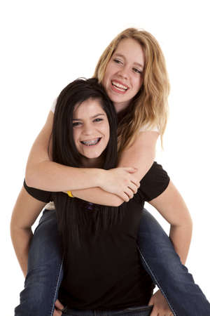 A teen girl giving her friend a piggy back ride laughing.の写真素材