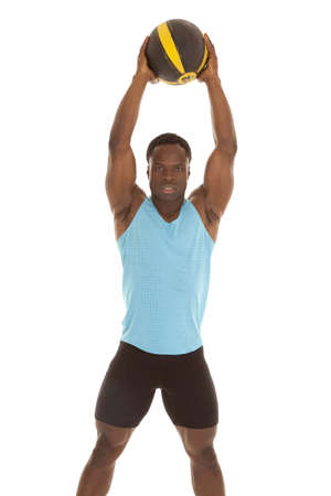 A man holding up his medicine ball up in the air with a serious expression  on his faceの写真素材