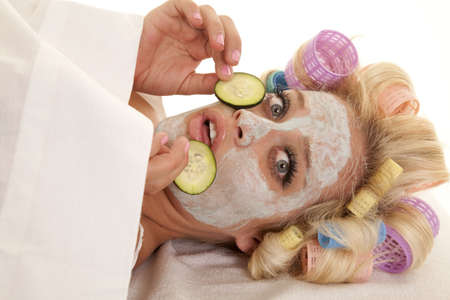 A woman has curlers in her hair and a cream face mask holding a cumber slice.の写真素材