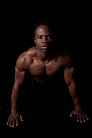 A man doing a push up showing off his muscles on a black background.