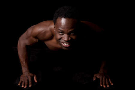 A man doing a push up showing off his muscles on a black background.の写真素材