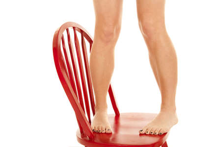 A woman standing on the seat of a red chair with her bare feet.の写真素材