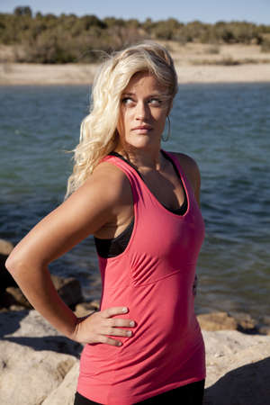A woman in a pink tank is standing by the water looking to the side.の写真素材