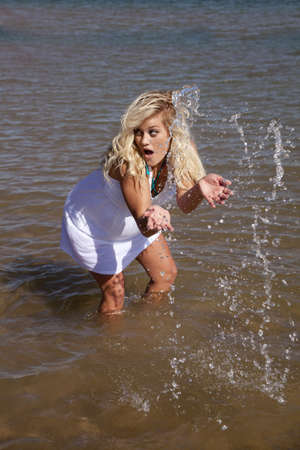 A woman in a white dress is splashing water and looks shocked.の写真素材