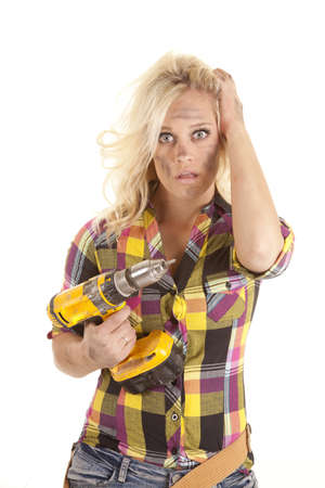 A woman is holding a drill with one hand while the other is in her hair.の写真素材