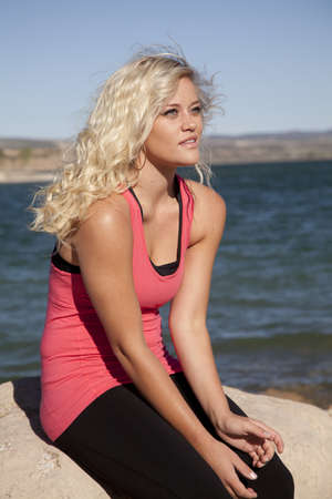 A woman is sitting on a rock by the water looking serious. の写真素材