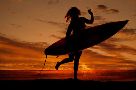A silhouette of a woman holding on to her surf board running on the beach.の写真素材