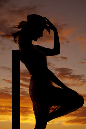 a silhouette of a woman leaning up against a post with a beautiful sunset in the background.の写真素材