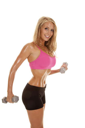 A woman working out with weights with a smile on her face and sweat dripping off of her body.の写真素材