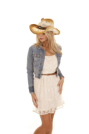 A woman standing in her dress, denim jacket, and hat looking down.の写真素材