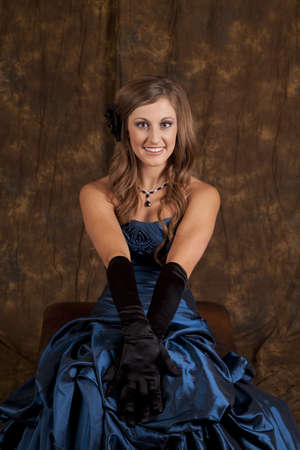 A teen girl sitting in her blue formal gown with a smile on her face.の写真素材