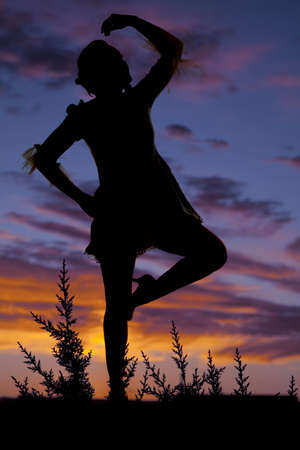 A silhouette of a woman dancing with a colorful sky behind her.の写真素材