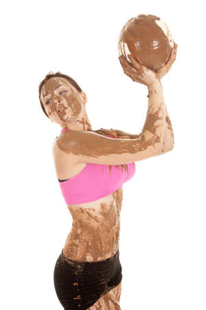 A woman looking over her shoulder holding up a volleyball that is covered in mudの写真素材