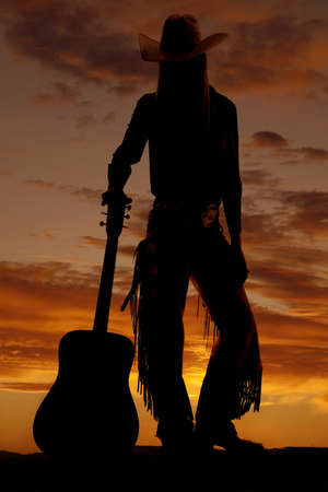 A cowgirl silhouette standing next to her guitar.の写真素材