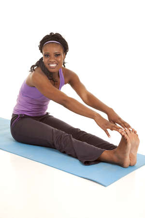a woman sitting on her mat stretching out her legs with a smile on her face.の写真素材